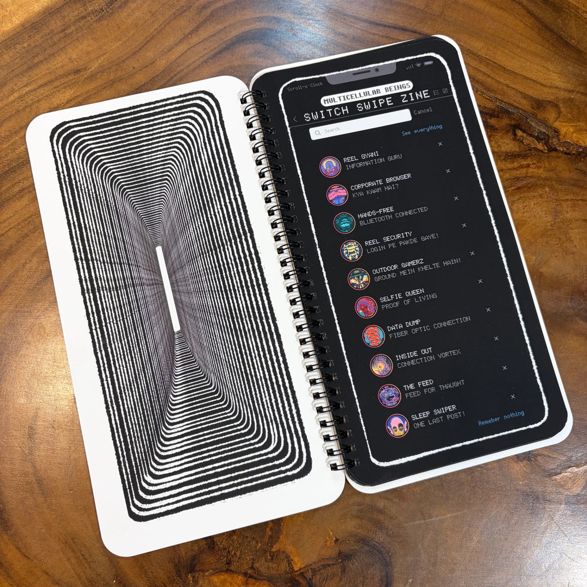A spiral-bound notebook or journal lies open on a wooden table. The left page shows a black-and-white tunnel-like striped pattern, and the right page displays a dark interface with a list of connected devices under the heading 'Switch Wide Zine.